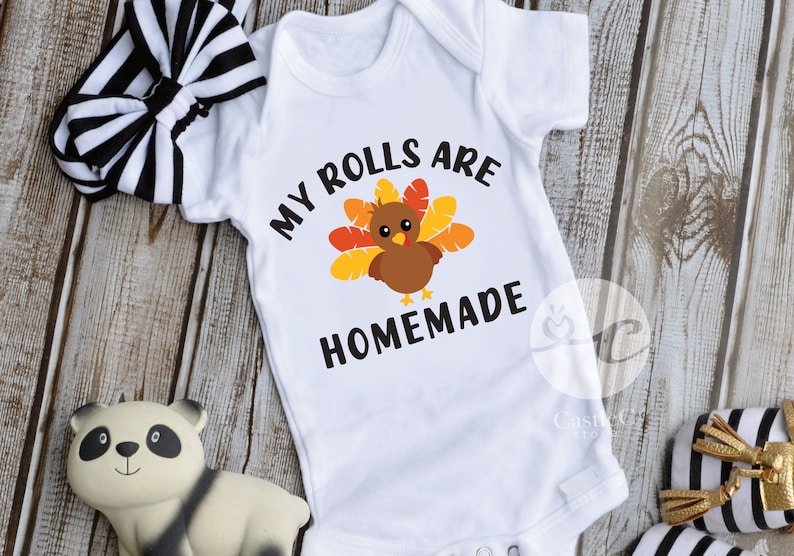 May include: White baby onesie with a brown turkey graphic and the text "My rolls are homemade".