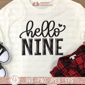 Puede incluir: Una camiseta blanca con texto negro que dice "hello nine" con un peque&ntilde;o coraz&oacute;n sobre la palabra "hello".