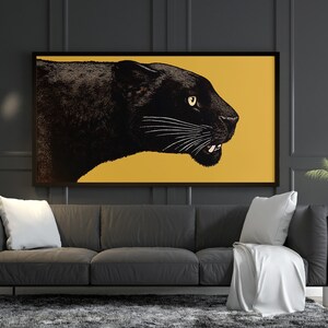 K&ouml;nnte beinhalten: Ein schwarzer Panther vor gelbem Hintergrund in einem gerahmten Druck, der &uuml;ber einem grauen Sofa mit wei&szlig;en Kissen h&auml;ngt.