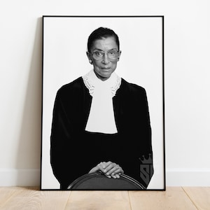 May include: Black and white portrait photograph of a woman wearing a black robe and white collar, with glasses and short hair. She is sitting with her hands clasped in her lap.