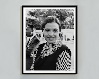 May include: Black and white framed portrait of Rosa Parks, smiling and wearing glasses, a striped blouse, and a dark vest. Martin Luther King Jr. is visible in the background. The photograph is a historical image.