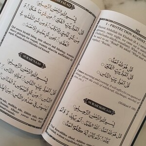 May include: A page from a book with Arabic text in black ink on a white background. The text is divided into two columns. The left column is titled "Surah Naas" and the right column is titled "Protection Against".