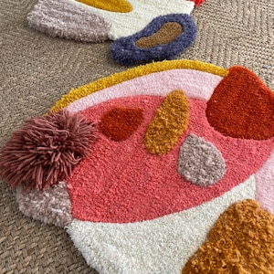 May include: Two colorful, abstract, hand-woven rugs with a variety of textures and shapes. The rugs are made with different colors of yarn, including pink, orange, yellow, brown, and white.