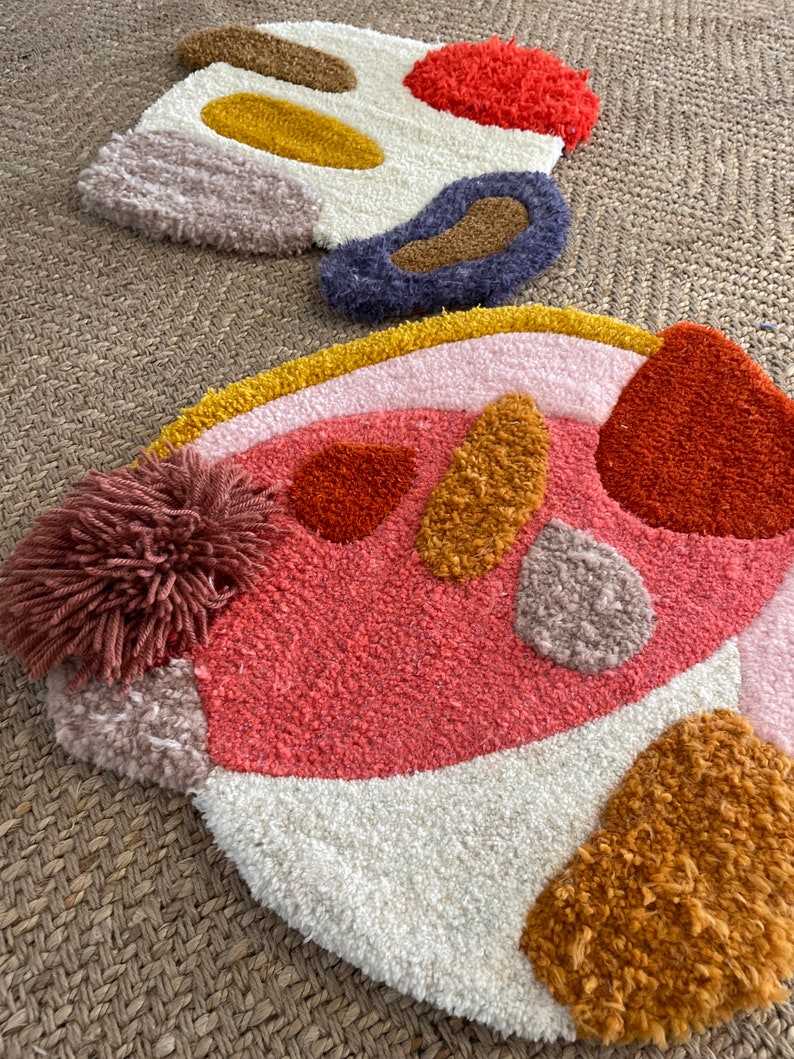 May include: Two colorful, abstract, hand-woven rugs with a variety of textures and shapes. The rugs are made with different colors of yarn, including pink, orange, yellow, brown, and white.