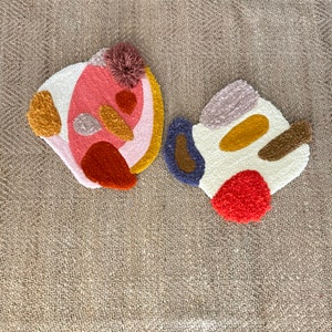 May include: Two abstract shaped rugs with a variety of colors and textures. The rugs are made of a fluffy material and have a variety of shapes and colors, including pink, red, orange, yellow, brown, blue, and white.