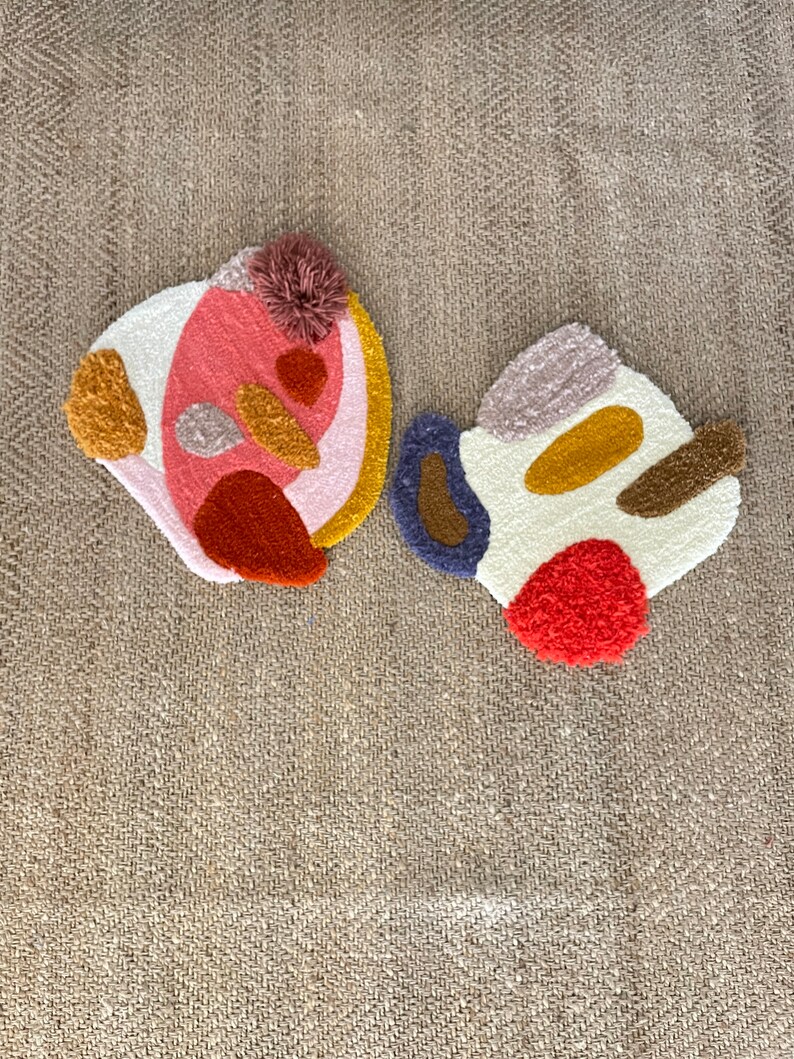 May include: Two abstract shaped rugs with a variety of colors and textures. The rugs are made of a fluffy material and have a variety of shapes and colors, including pink, red, orange, yellow, brown, blue, and white.