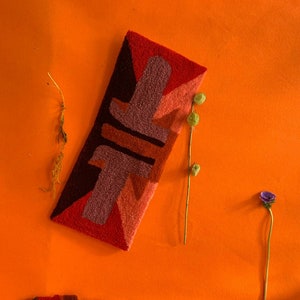 Pu&ograve; includere: Un tappeto astratto colorato con forme geometriche in tonalit&agrave; di rosso, arancione, marrone e rosa. Il tappeto &egrave; su uno sfondo arancione brillante.