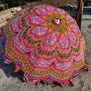 Może przedstawiać: Kolorowy, okrągły parasol w odcieniach r&oacute;żu i zieleni, z misternymi haftami i cekinami. Parasol jest wykonany z tkaniny i ma drewniany uchwyt.