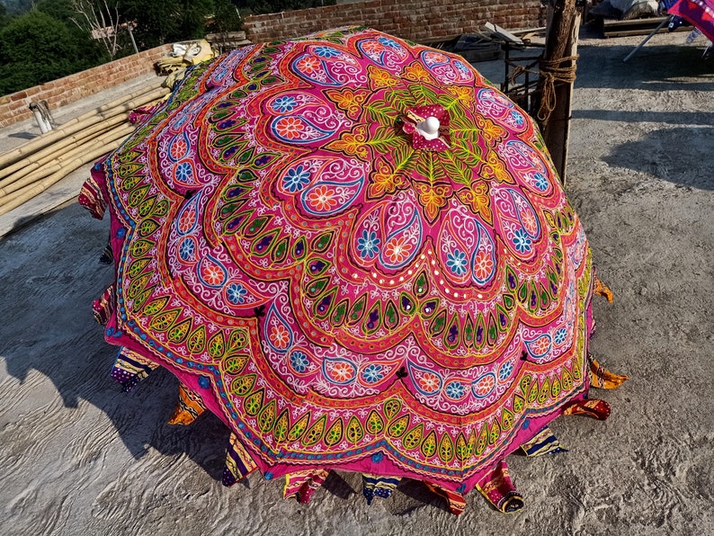 Może przedstawiać: Kolorowy, okrągły parasol w odcieniach r&oacute;żu i zieleni, z misternymi haftami i cekinami. Parasol jest wykonany z tkaniny i ma drewniany uchwyt.
