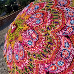 Może przedstawiać: R&oacute;żowy, okrągły parasol z tkaniny z kolorowymi haftami i akcentami lustrzanymi. Parasol jest ozdobiony wzorami paisley i motywami kwiatowymi.