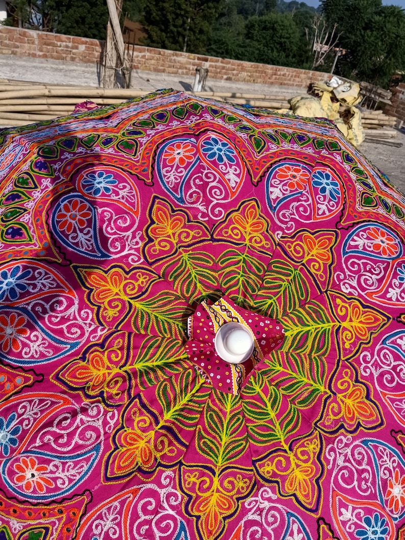 Może przedstawiać: R&oacute;żowy parasol z kolorowymi haftami przedstawiającymi wzory kwiatowe i paisley. Parasol jest wykonany z tkaniny i ma białe centrum.