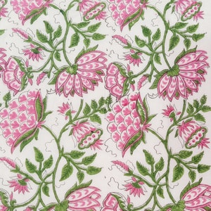 May include: A white textile with a repeating floral pattern. Large pink flowers with green accents and stems are evenly spaced across the fabric. The leaves are a vibrant green, and the overall design is symmetrical.