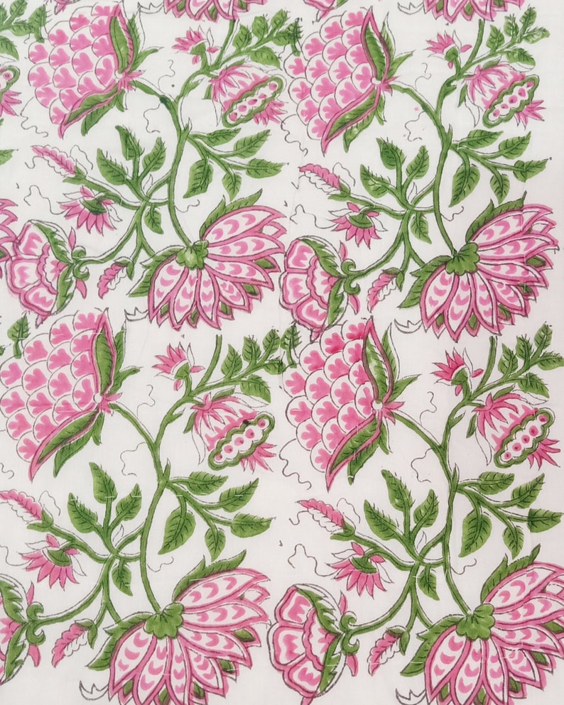 May include: A white textile with a repeating floral pattern. Large pink flowers with green accents and stems are evenly spaced across the fabric. The leaves are a vibrant green, and the overall design is symmetrical.