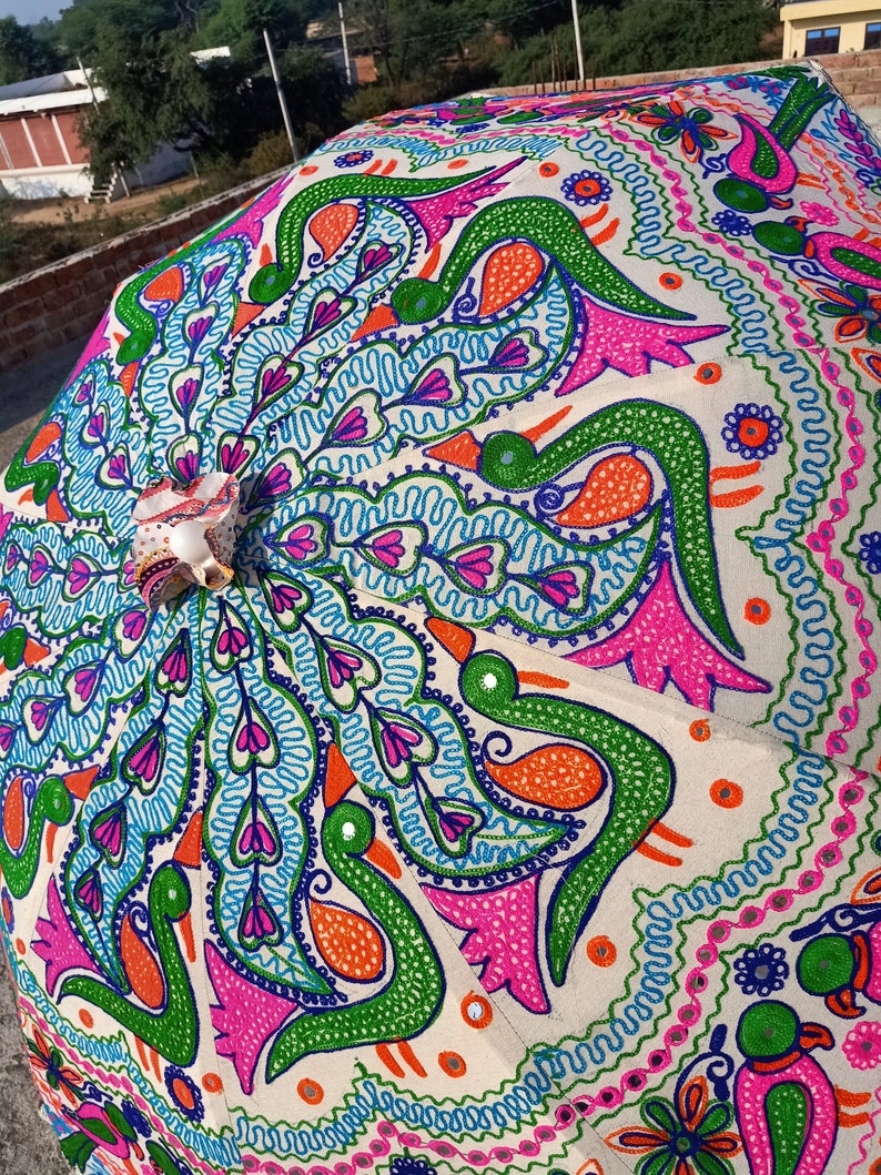 Może przedstawiać: Ozdobny, otwarty parasol z kremową tkaniną. Tkanina jest misternie haftowana żywym wzorem pawia w odcieniach zieleni, r&oacute;żu, pomarańczy i błękitu. Parasol jest pięknym przykładem rzemiosła.