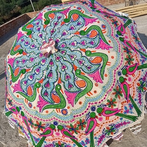 Może przedstawiać: Kolorowy, otwarty parasol z żywym, ręcznie malowanym wzorem. Parasol ma kremowe tło z powtarzającym się wzorem ptak&oacute;w, kwiat&oacute;w i wirujących linii w odcieniach r&oacute;żu, zieleni, niebieskiego i pomarańczowego. Krawędzie są ząbkowane.