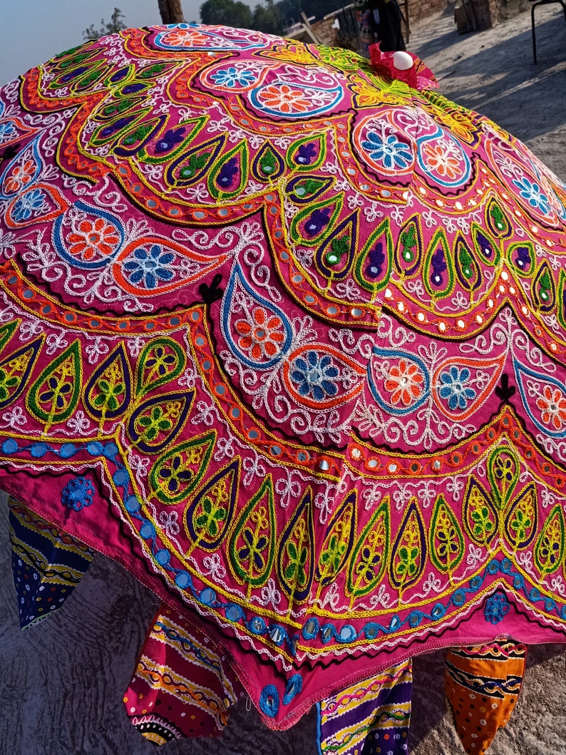 Może przedstawiać: R&oacute;żowy i wielokolorowy parasol z misternymi haftami i akcentami lustrzanymi. Parasol jest ozdobiony wzorami kwiatowymi i paisley.