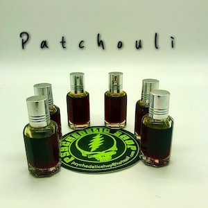 May include: Small glass bottles filled with a dark amber liquid, topped with silver caps. The word "Patchouli" is written above the bottles. A round sticker with a green logo and the text "PSYCHEDELIC SHOP" is at the bottom.