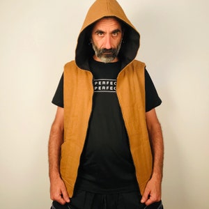 Può includere: Un gilet marrone con cappuccio, cerniera nera e una maglietta nera sotto. La maglietta ha la parola "PERFECT" stampata due volte.
