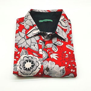 Puede incluir: Camisa roja doblada con cuello negro y un llamativo estampado floral en blanco y negro. La camisa tiene botones de madera y el texto "PSYCHEDELICSHOP" en el cuello.