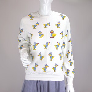 May include: White sweatshirt with a pattern of blue, yellow, and red ducks wearing winter hats.
