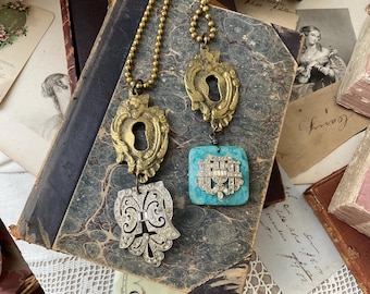 May include: Two gold keyhole pendant necklaces with a turquoise and rhinestone pendant. The necklaces are displayed on a vintage book with a white lace overlay.