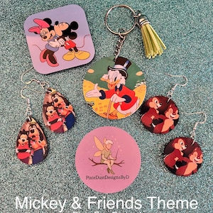 May include: A collection of Mickey & Friends themed accessories, including earrings, a keychain, and a puzzle piece. The items feature colorful cartoon characters on a glittery teal surface. The text "Pixie DustDesignsByD" is visible.