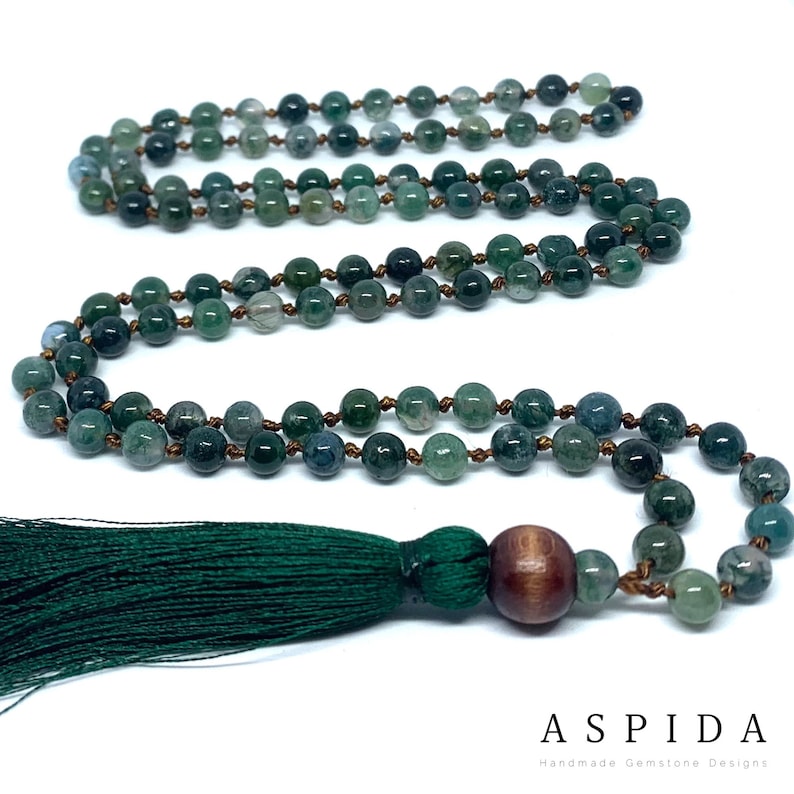 May include: A green agate mala necklace with a wooden bead and a green tassel. The necklace is made of 108 beads and is approximately 18 inches long.