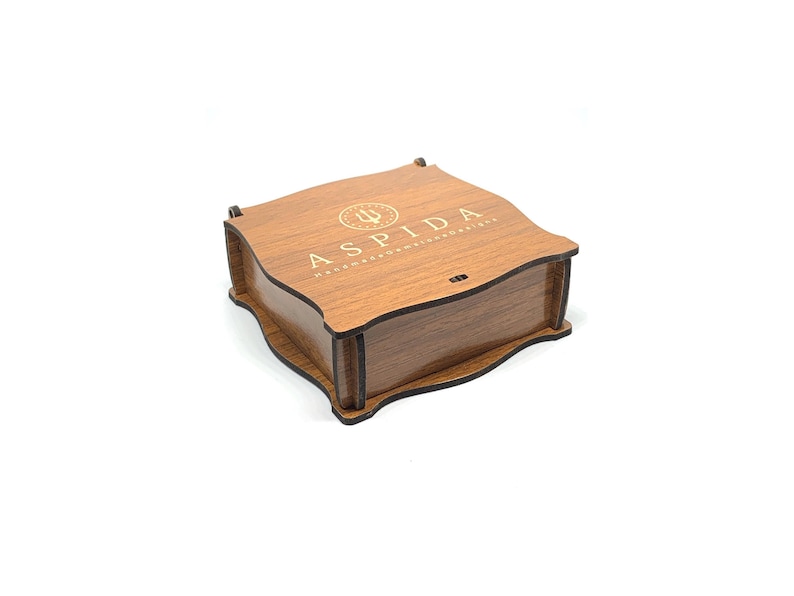 May include: A wooden box with a dark brown stain and a gold inscription that reads "ASPIDA  HANDMADE WITH PASSION & DETAIL".
