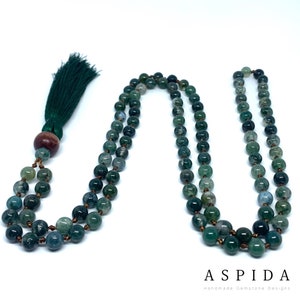 May include: A green agate mala necklace with a green tassel. The necklace is made of 108 beads and has a wooden bead at the end.