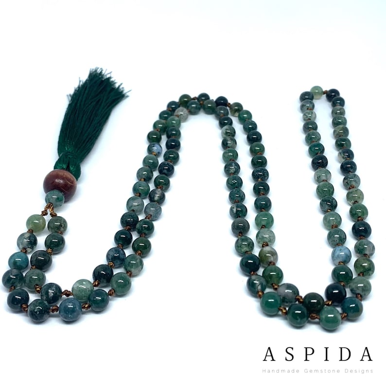 May include: A green agate mala necklace with a green tassel. The necklace is made of 108 beads and has a wooden bead at the end.