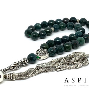 May include: A green and silver gemstone prayer beads, or rosary, with a silver tassel. The beads are made of green aventurine, a type of quartz. The tassel is made of silver and has a decorative design. The beads are strung on a silver cord. The beads are approximately 1 cm in diameter. The tassel is approximately 10 cm long. The beads are used for prayer and meditation.
