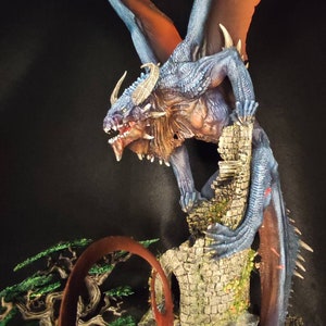 May include: A blue and red dragon figurine perched on a stone tower, with a smaller figure standing below. The dragon's wings are spread wide, and its tail curls around the tower.