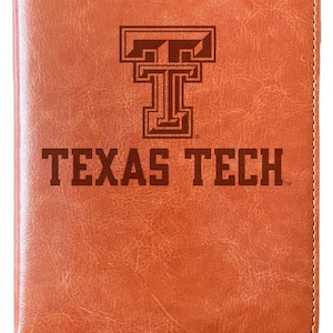 May include: A brown leather journal with a bookmark. The front cover features a brown leather Texas Tech logo and the words "TEXAS TECH" in brown.