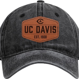 May include: A black, distressed-look baseball cap with a curved brim. The cap features a brown leather patch with the text "UC DAVIS" and "EST. 1908". The patch has a university logo above the text.