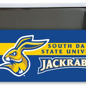 May include: A blue and yellow magnet featuring the South Dakota State University logo. The logo includes a yellow jackrabbit mascot with a blue outline and the words "South Dakota State University" and "Jackrabbits" in yellow.