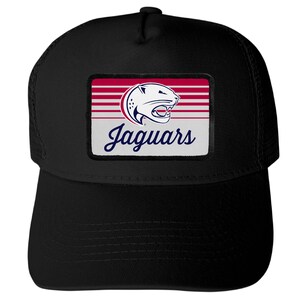 May include: A black trucker hat featuring a rectangular patch on the front. The patch displays a stylized jaguar head logo above the word Jaguars in blue script, set against a background of horizontal red and white stripes on a white field.