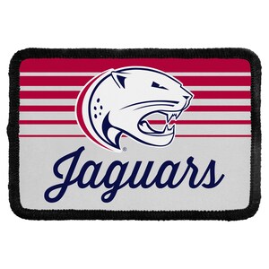 May include: A rectangular embroidered patch with a black stitched border. The design features a white jaguar head logo with dark blue accents, set against a background of horizontal red and white stripes above a solid light gray base with the word Jaguars.