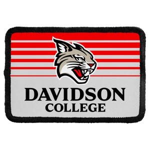 May include: A rectangular embroidered patch with a black border. The design features horizontal red and white stripes, a graphic of a wildcat head with a red mouth, and the black text DAVIDSON COLLEGE centered on a light gray background.