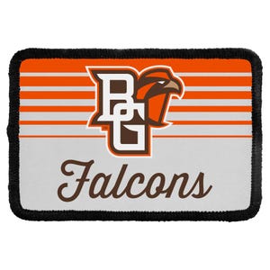 May include: A rectangular embroidered patch with a black stitched border. The design features horizontal orange and white stripes, a brown and white BG logo with a falcon head icon, and the word Falcons in brown script lettering below the logo.