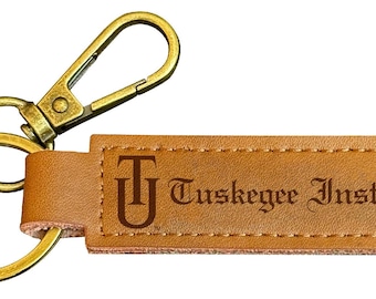 May include: A brown leather keychain with a gold metal key ring and a clasp. The keychain has a rectangular leather tag with the text "Tuskegee Institute" and the letter "T" in a stylized font.