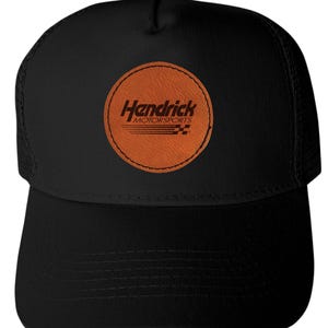 May include: Black trucker hat with a curved brim and mesh back. The front features a circular patch with the text "Hendrick Motorsports" in a stylized font, with a checkered flag design.