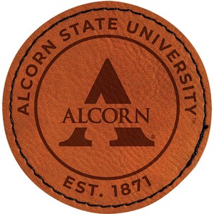 May include: A round, brown leather patch with the words "ALCORN STATE UNIVERSITY" in a circular pattern. The university's logo, a stylized "A", is in the center, with "ALCORN" below it. The text "EST. 1871" is at the bottom. Black stitching outlines the patch.