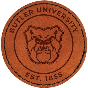 May include: A round, brown leather patch featuring the words "BUTLER UNIVERSITY" in a circular pattern. The center displays a bulldog graphic, with "EST. 1855" below. The edge is stitched with black thread, creating a collegiate emblem.
