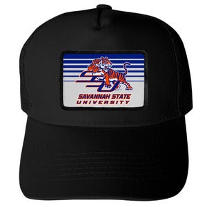 May include: A black baseball cap featuring a rectangular patch on the front. The patch displays a blue and white striped background with an orange and black tiger graphic above the text SAVANNAH STATE UNIVERSITY in orange and blue letters.