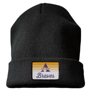 May include: A black knit beanie featuring a rectangular patch on the front cuff. The patch displays horizontal gold and white stripes, a purple letter A, the word ALCORN in purple, and the word Braves in purple script lettering on a white background.