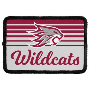 May include: A rectangular patch with a black stitched border featuring a maroon and light gray striped background. Centered is a stylized gray and maroon wildcat head graphic above the maroon cursive text that reads Wildcats.