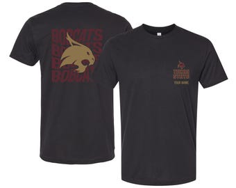 May include: Black t-shirt featuring the Texas State Bobcats logo on the front and back. The front displays the Texas State logo and the text "TEXAS STATE" and "YOUR NAME". The back has the word "BOBCATS" repeated with a bobcat head.