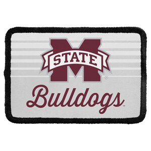 May include: A rectangular patch with a black stitched border featuring a white background with light gray horizontal stripes. The Mississippi State University logo is centered in maroon and white with the word Bulldogs in maroon script below.