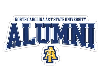 Könnte beinhalten: Ein weißer Aufkleber mit dem Text "NORTH CAROLINA A&T STATE UNIVERSITY" über dem Wort "ALUMNI" in Marineblau. Ein gold-blaues Logo befindet sich unter dem Wort "ALUMNI".