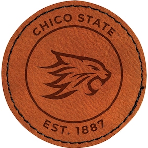 May include: A round, brown leather patch with the words "CHICO STATE" arched across the top. Inside a circle is a cougar head. The text "EST. 1887" is at the bottom. The patch is stitched with black thread.